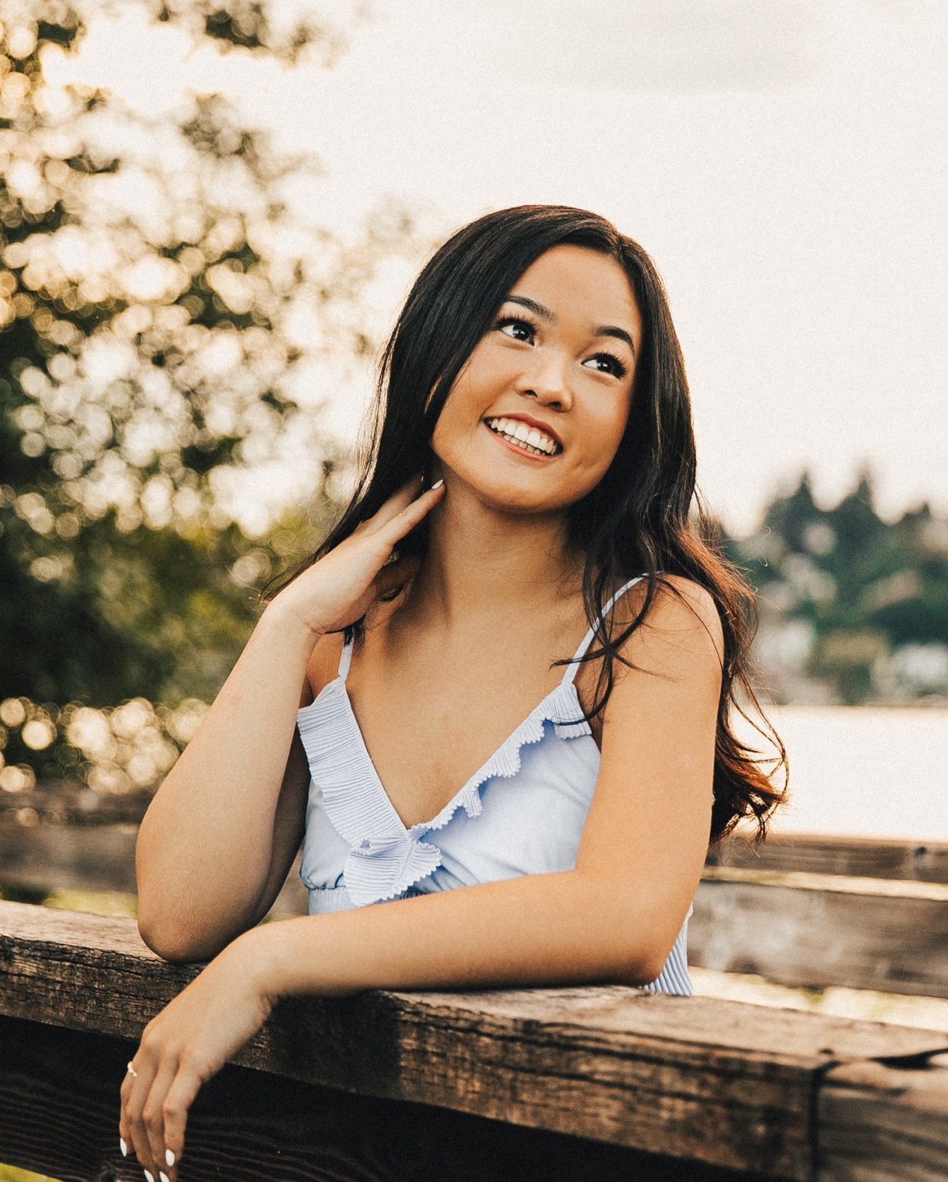 smiling girl leaning against wooden fence looking into the distance