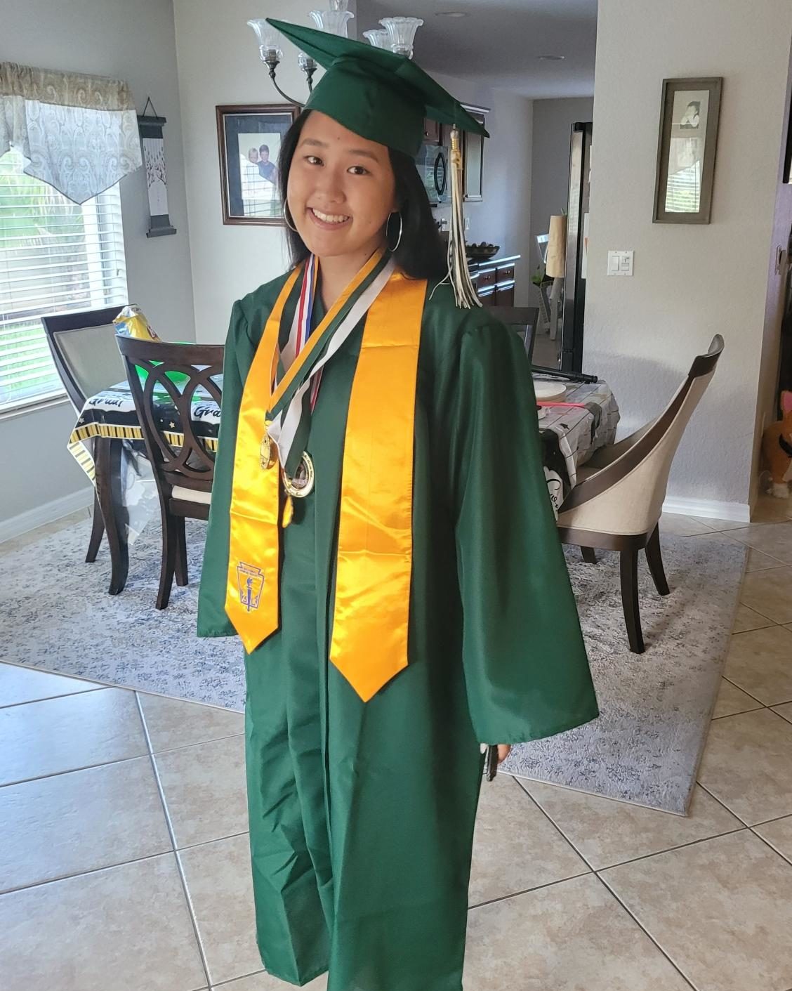 smiling girl standing in dining room wearing green graduation cap and gown