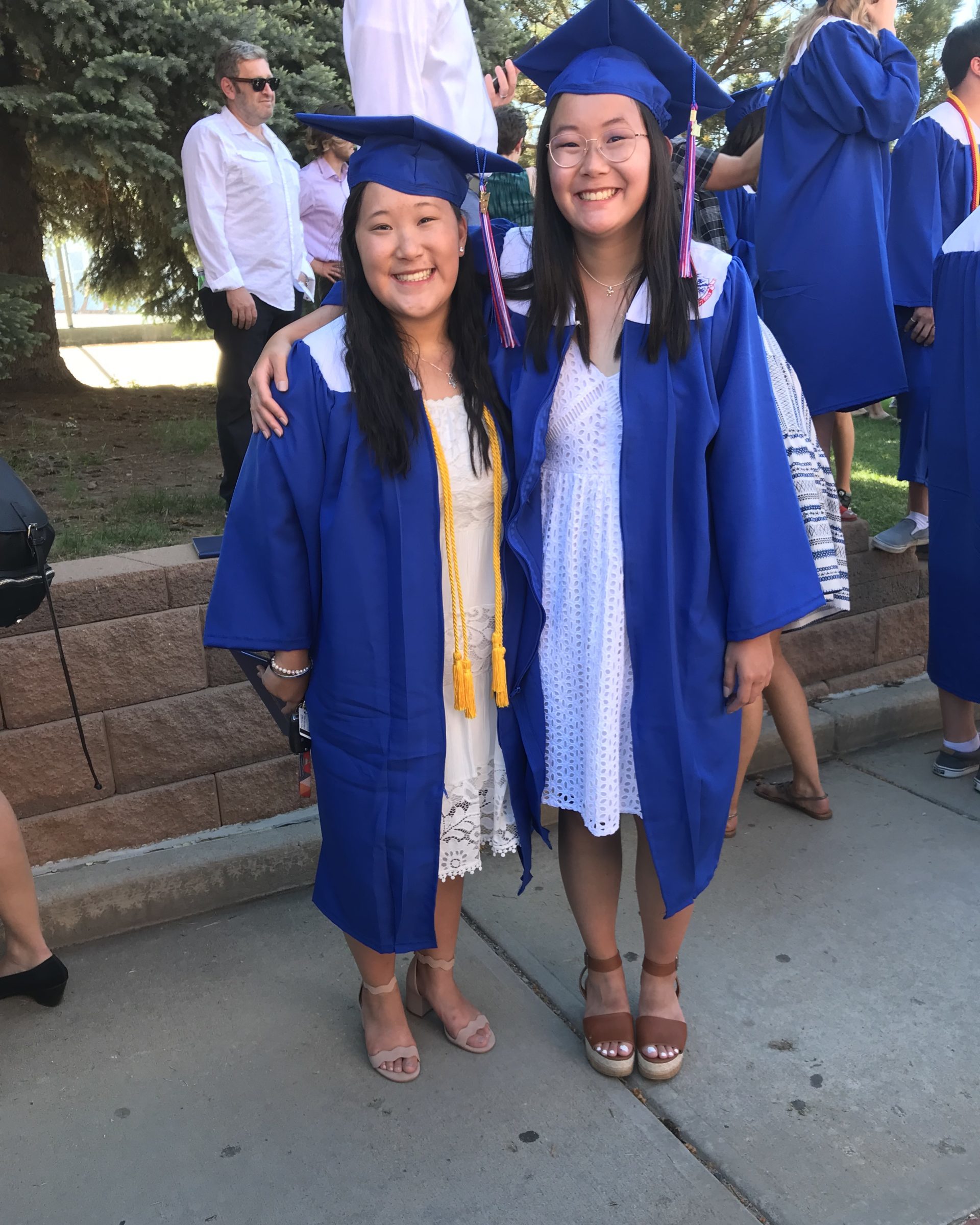 two sisters with their arms around each other wearing dresses and blue graduation cap and gowns