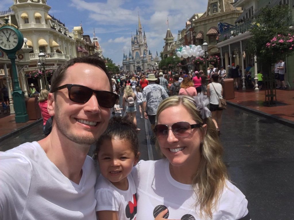 man and woman holding little girl in front of disneyland