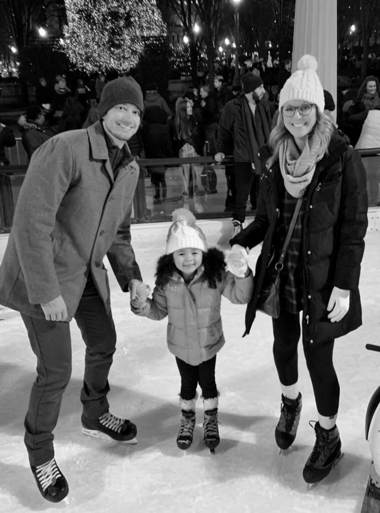 man and woman holding little girls hands wearing ice skates on ice rink