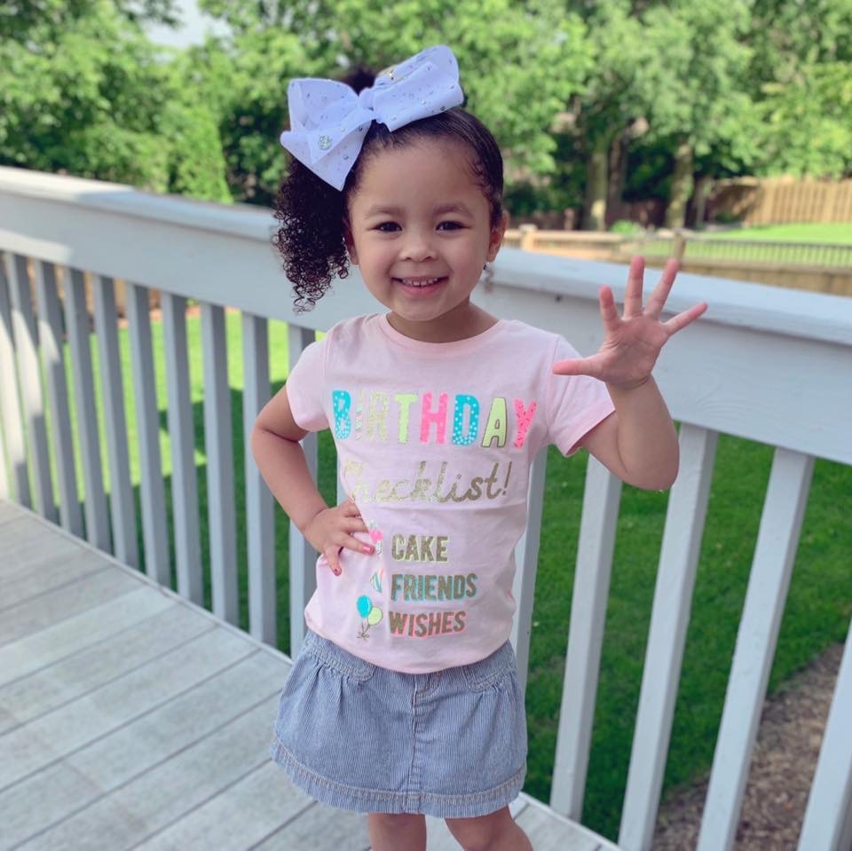 little girl wearing birthday shirt holding up five fingers