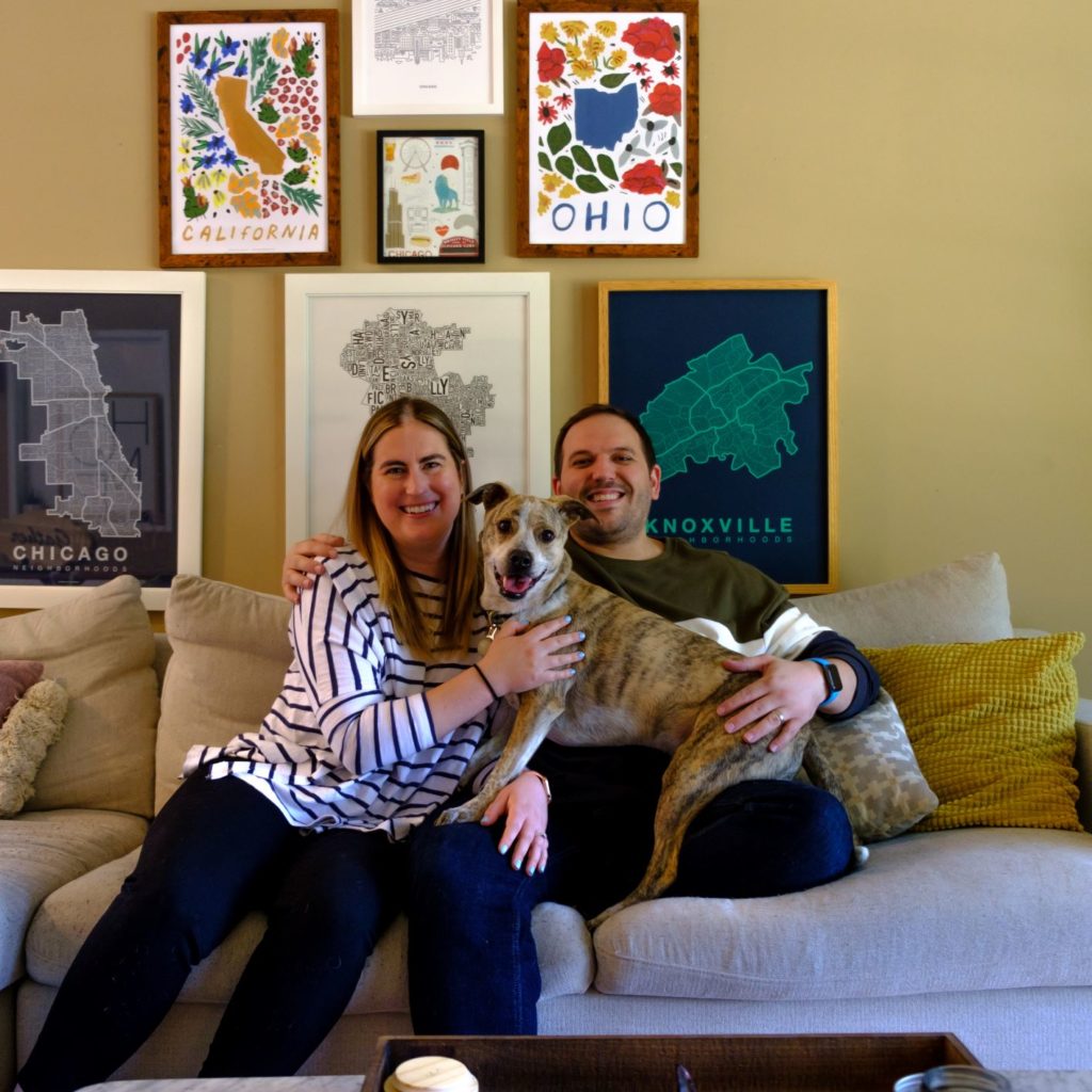 smiling man and woman holding brown dog and sitting on grey couch