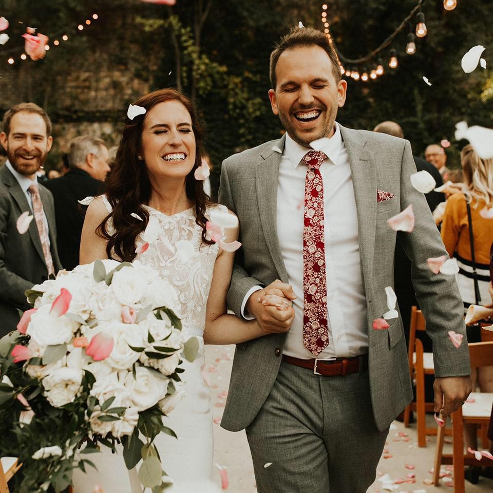 grinning man in grey suit and woman in wedding dress walking down the aisle
