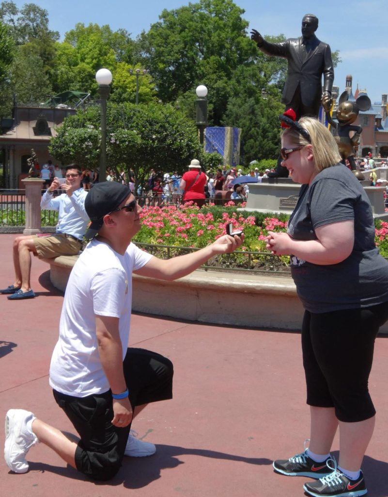 man on one knee proposing to woman wearing mickey ears
