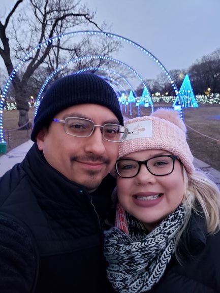 smiling man and woman in front of tunnel of christmas lights