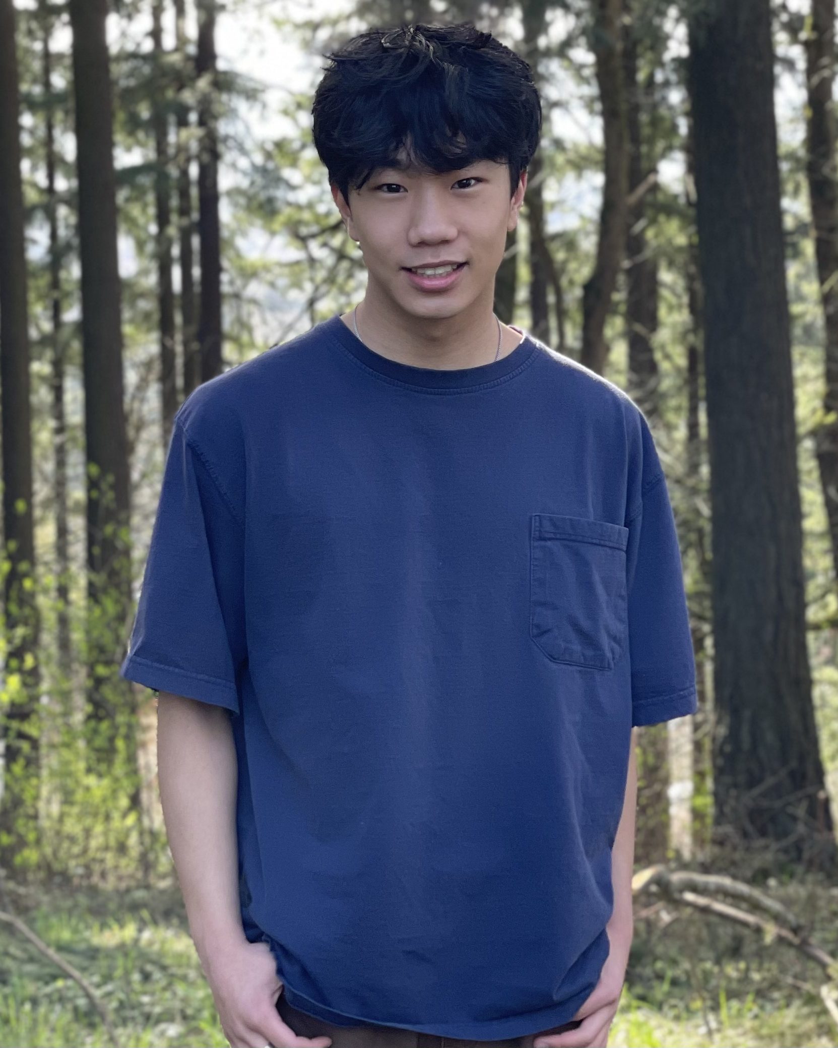 smiling man wearing blue shirt standing in forest