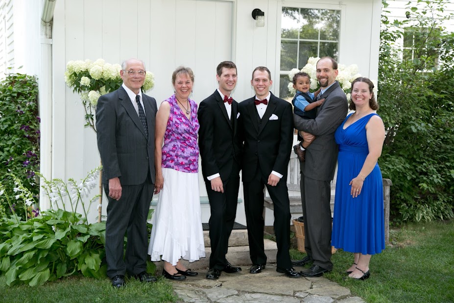 six smiling adults and one baby standing in wedding attire