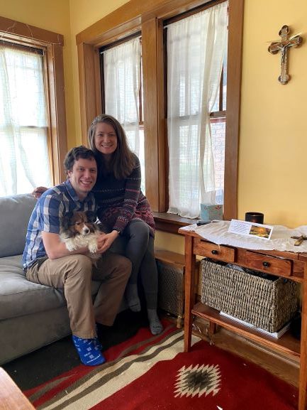 woman and man holding dog sitting on grey couch in front of windows