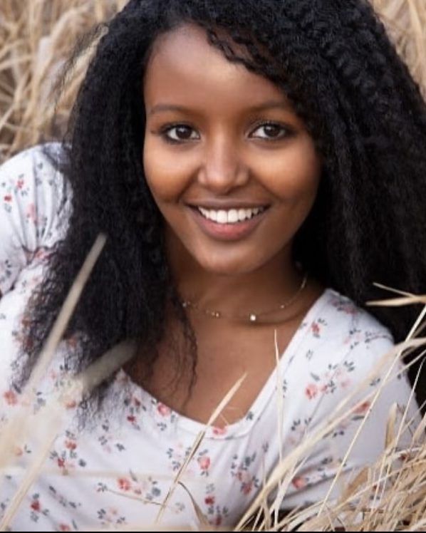 smiling girl with curly hair laying in wheat field