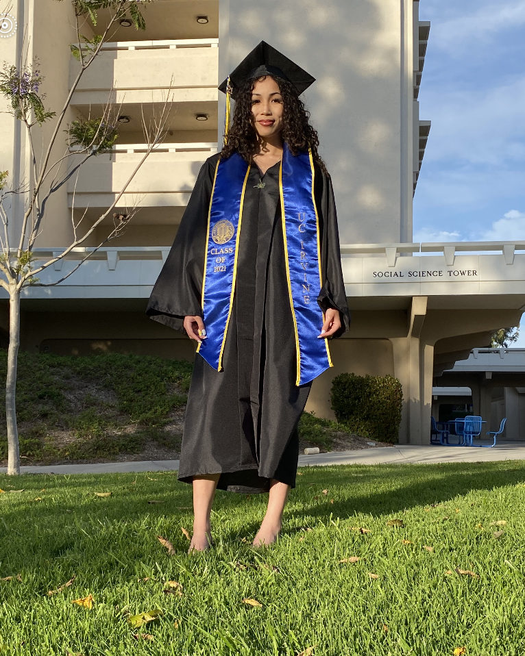 girl standing in black graduation cap and gown and blue sash that says "class of 2021 uc irvine"