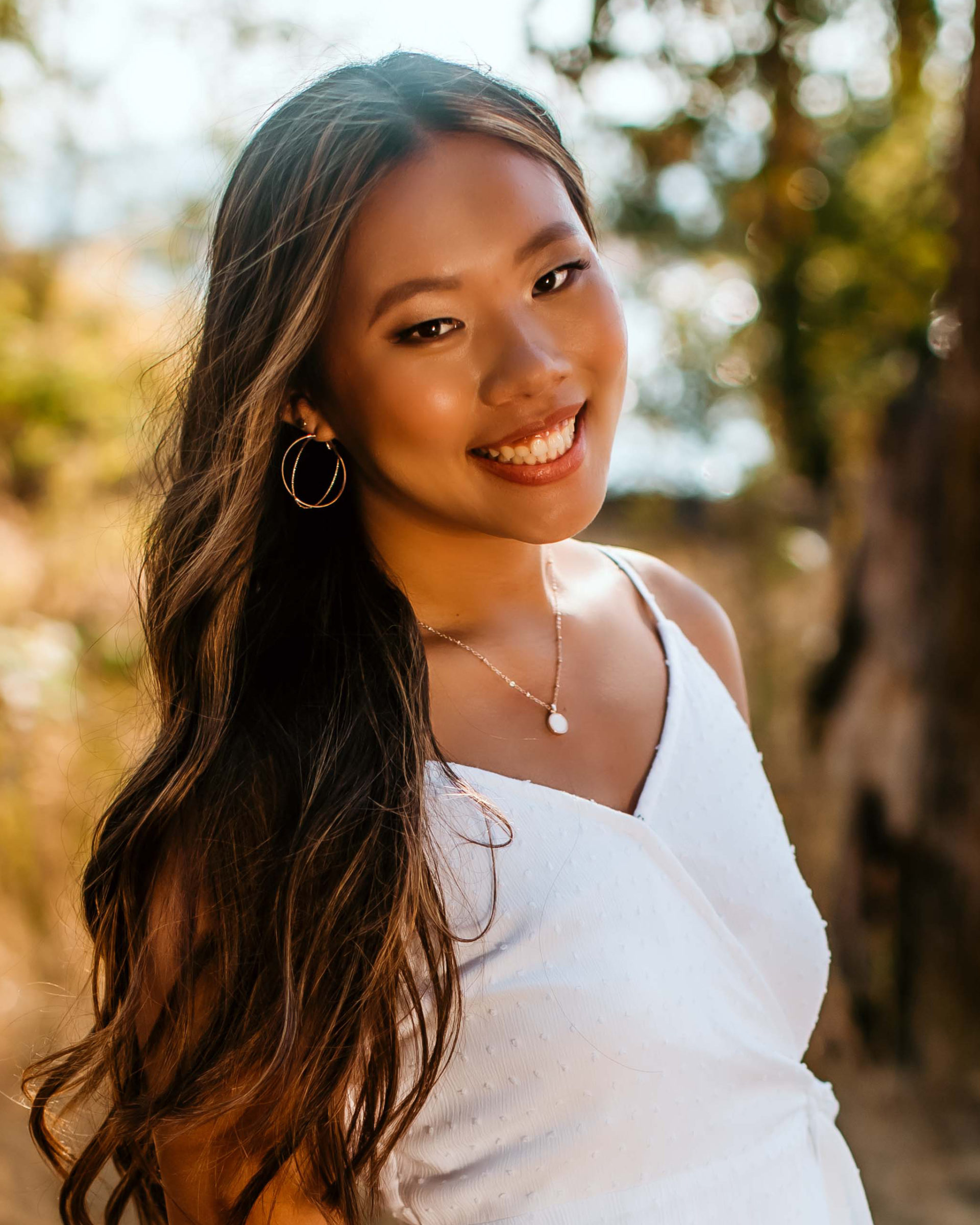 smiling girl with long wavy hair wearing hoop earrings and white dress