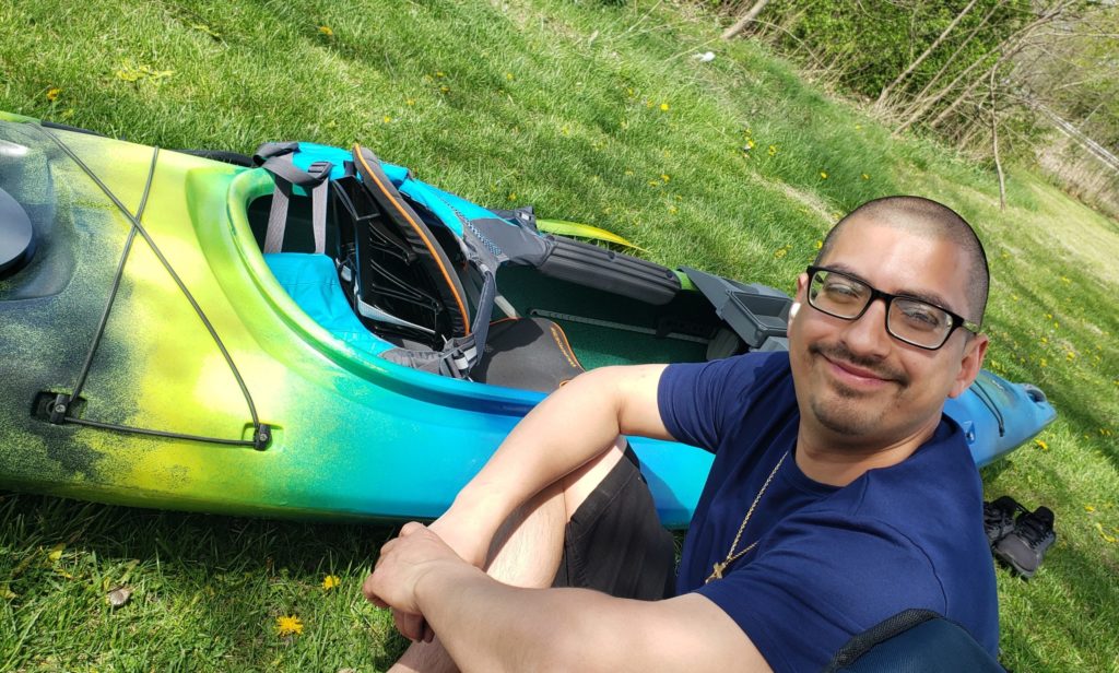 smiling man in front of green and blue kayak