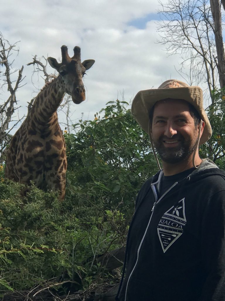 smiling man in hat standing in front of giraffe