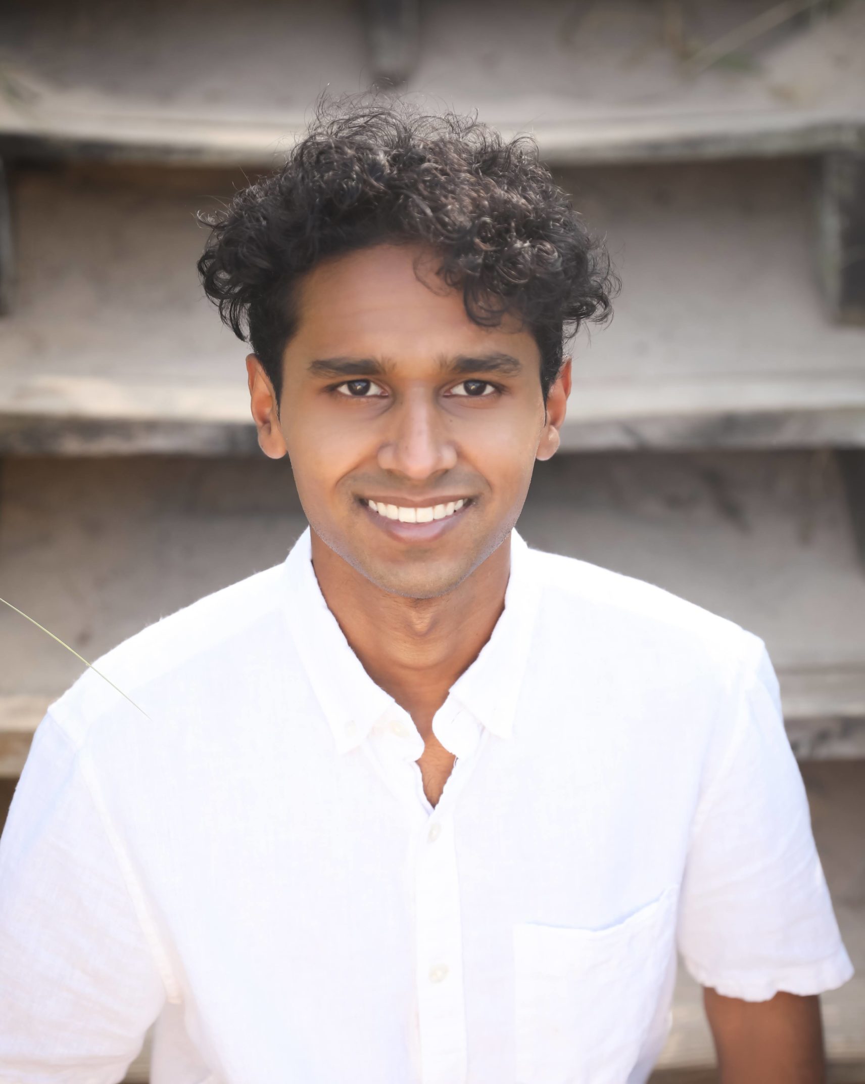 smiling man with curly hair wearing white short sleeve button up and sitting