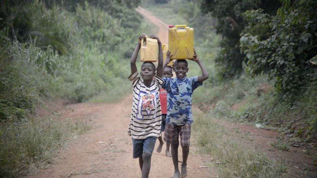 three boys in Uganda carrying water jugs above heads