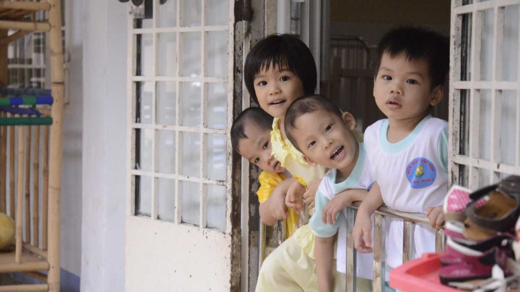 Siblings smile from doorway in Vietnam