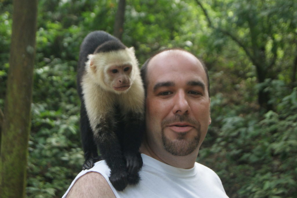 smiling man with monkey sitting on his shoulder