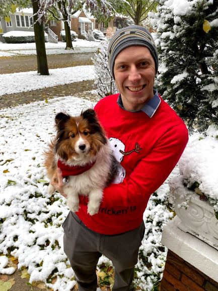 man in red sweater holding brown and white fluffy dog