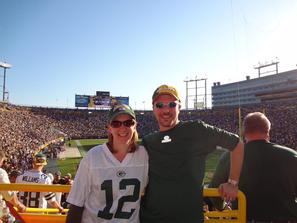 smiling man and woman wearing sunglasses and green and yellow clothing at football game