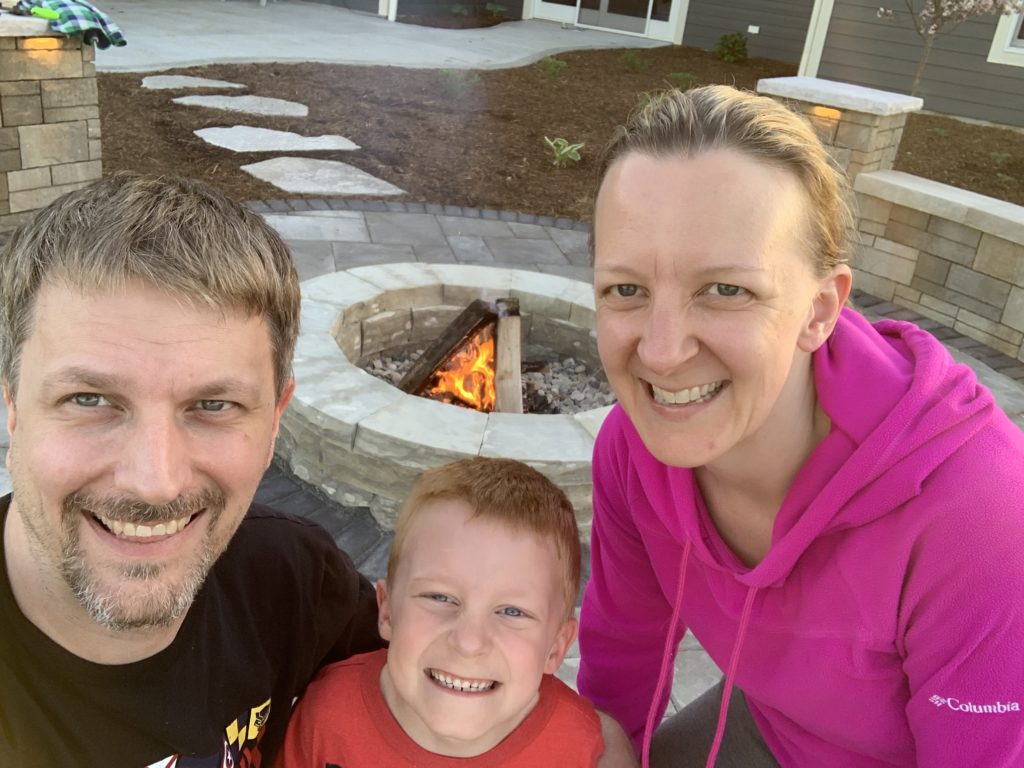 smiing man woman and boy in front of stone firepit