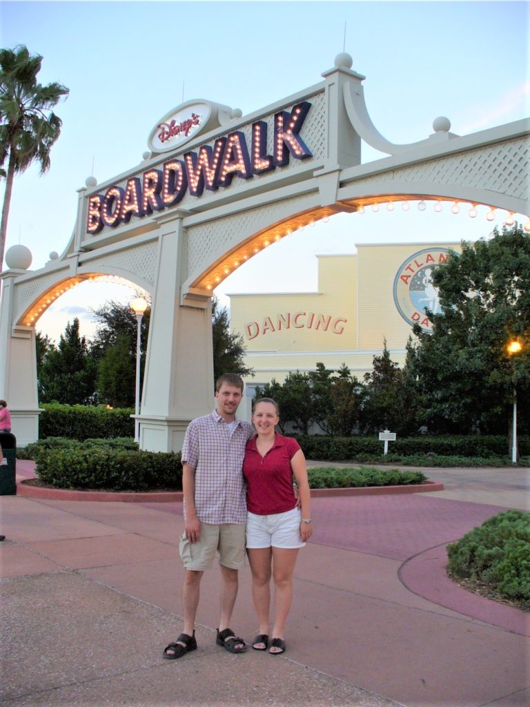 smiling man with arm around smiling woman under sign that says "disney boardwalk"