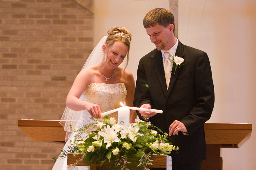 man in suit and woman in wedding dress lighting candle together