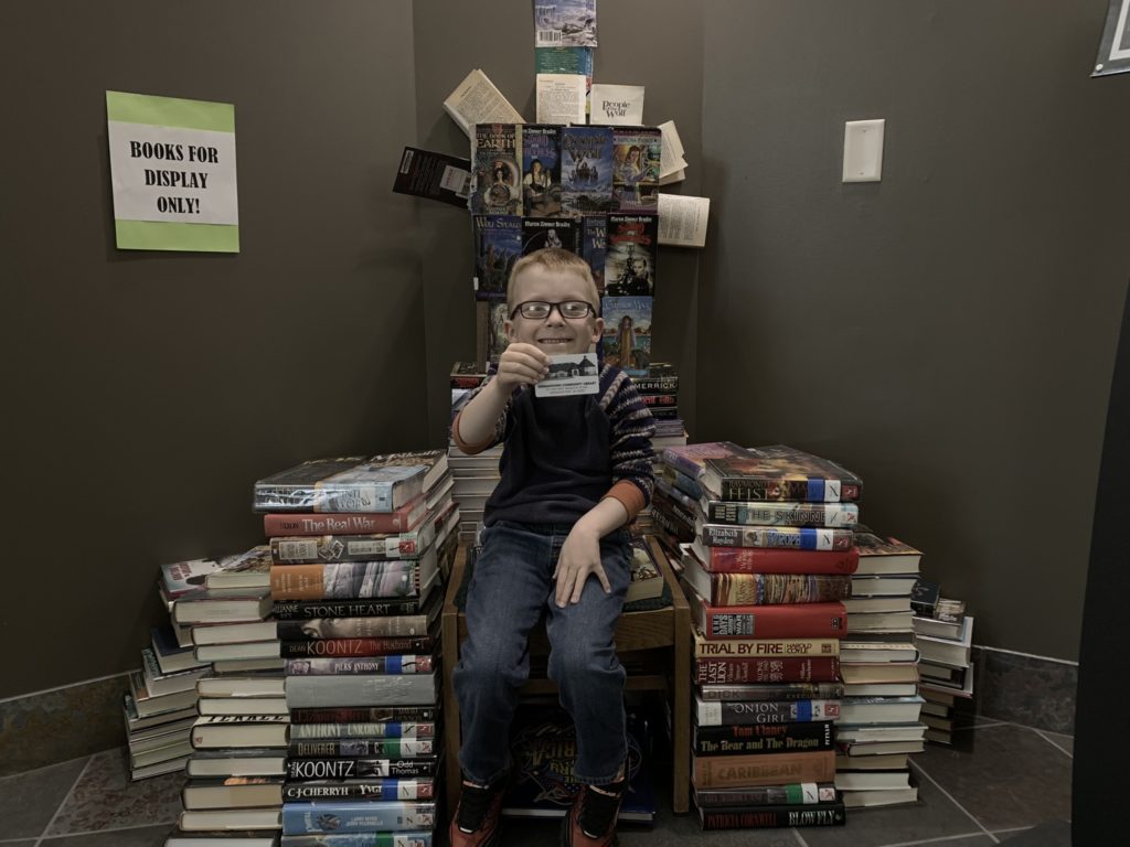 smiling boy in glasses sitting on chair made of books