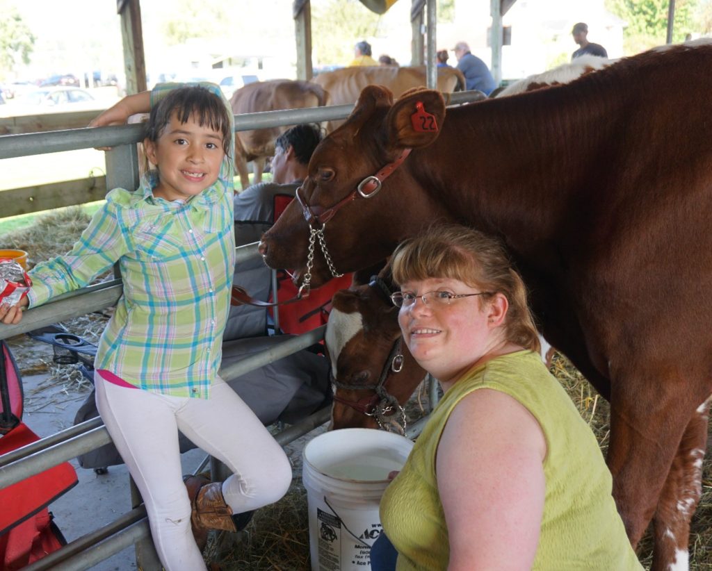 smiling girl and woman next to brown cow