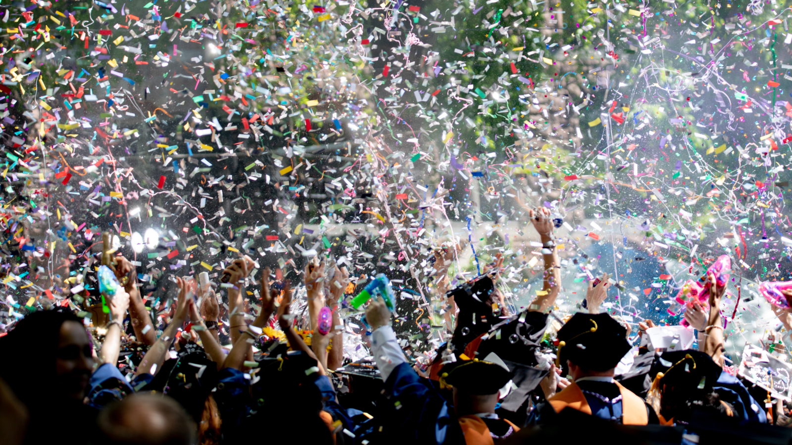 group of people in graduation caps and gowns throwing colorful confetti into the air