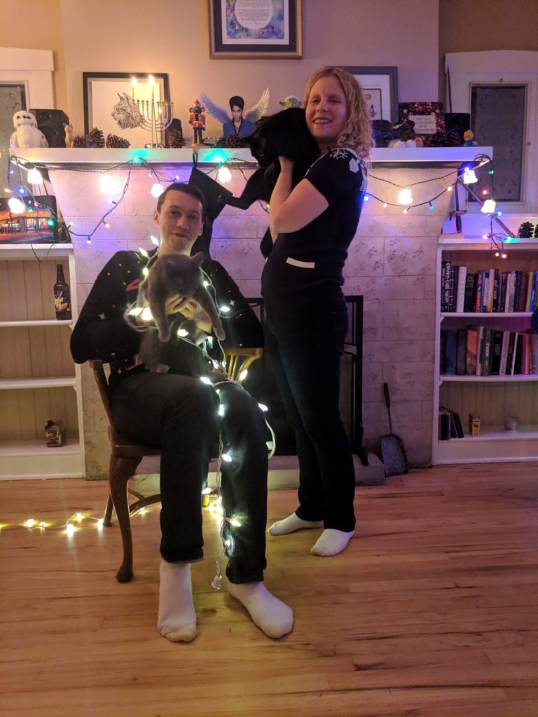 man and woman holding cats draped in christmas lights