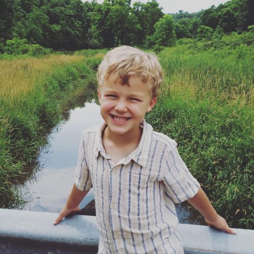 grinning blonde boy posing in front of creek