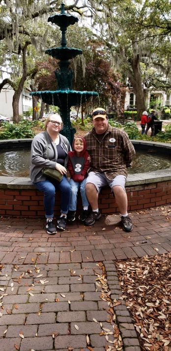 smiling mom dad and son sitting on a fountain