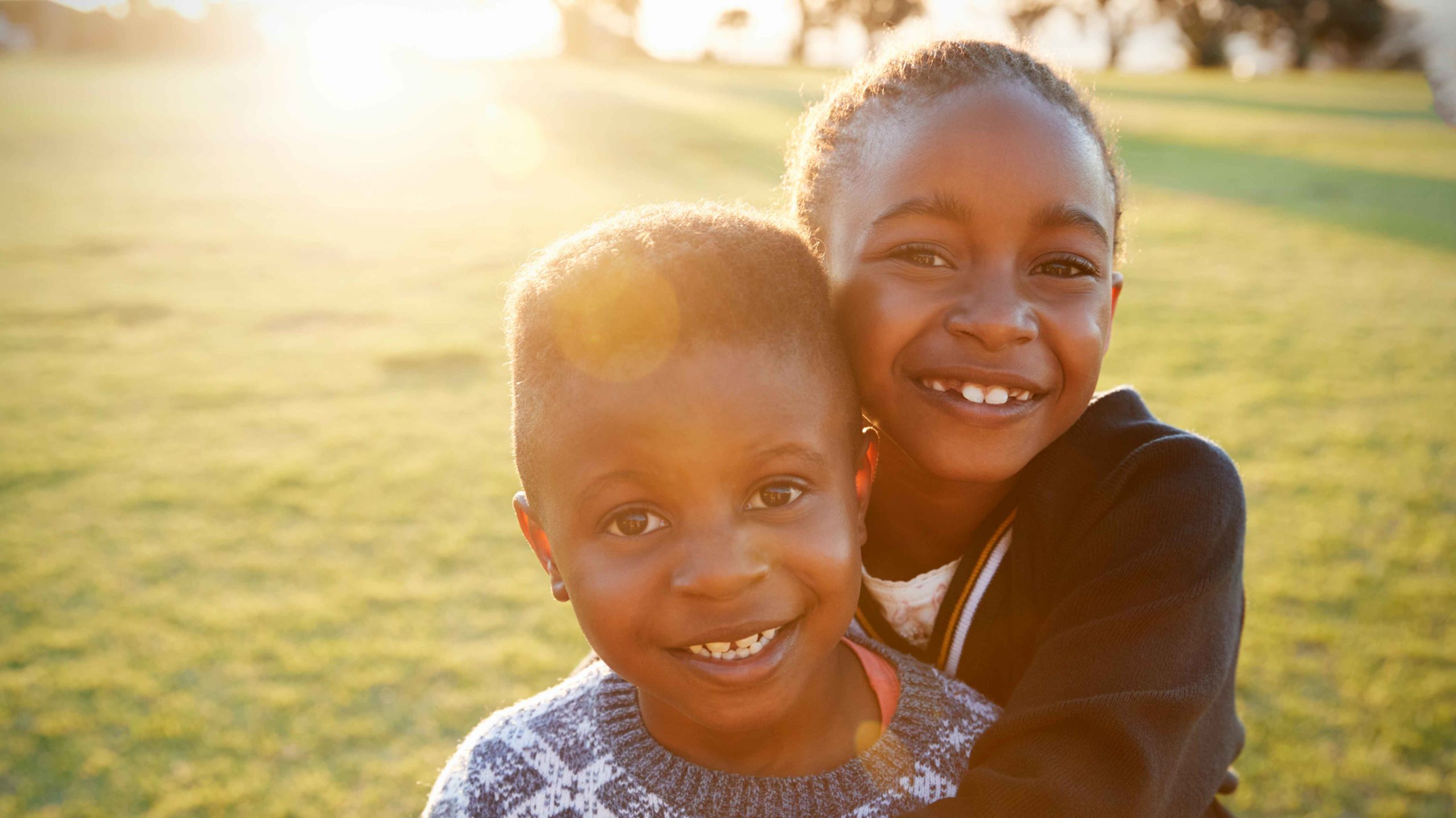 smiling girl with her arms around smiling boy, sibling support