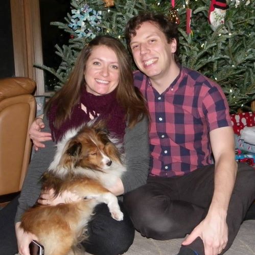 man and woman holding dog sitting in front of christmas tree