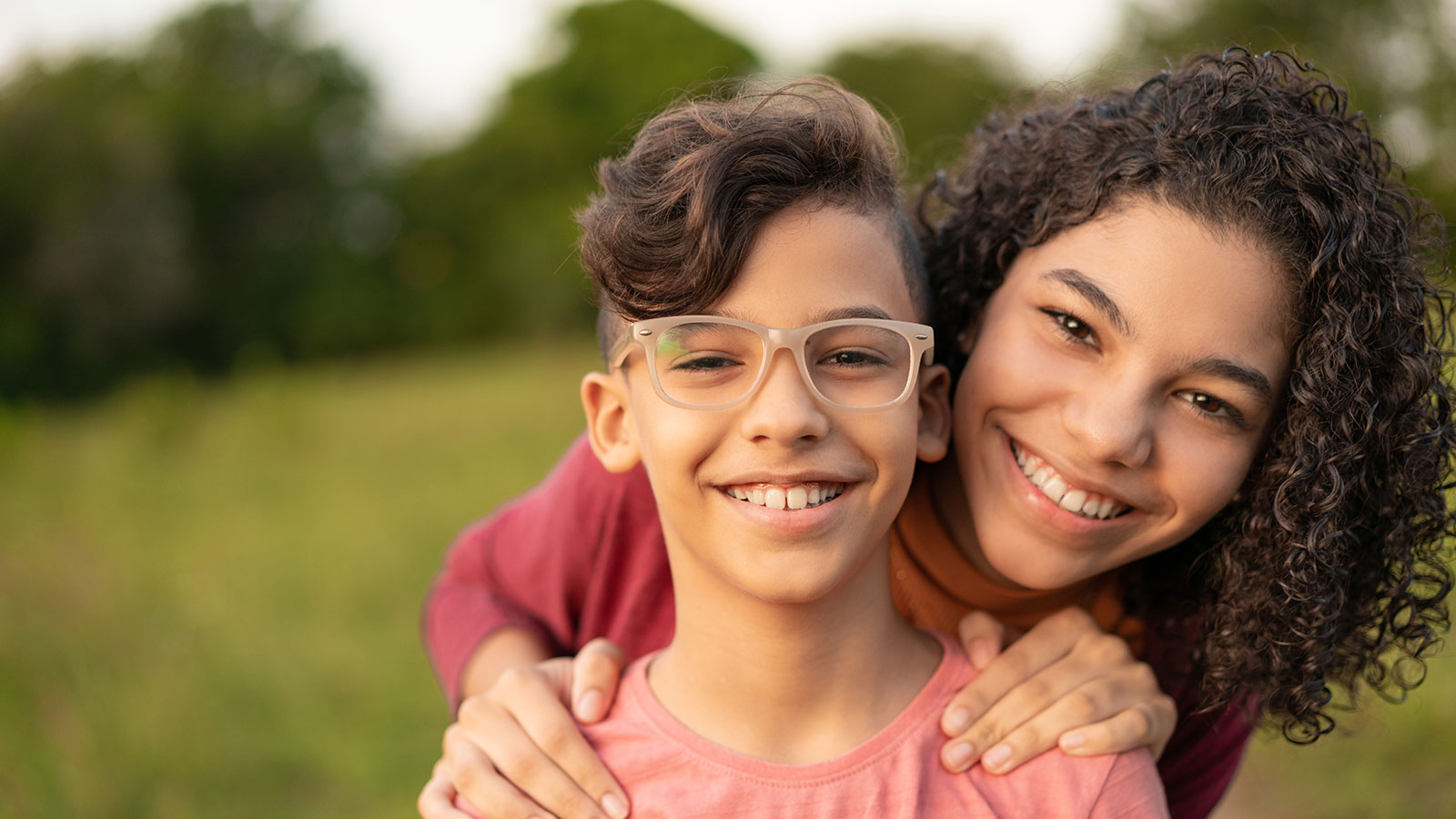 smiling older girl with her hands on little brother's shoulders