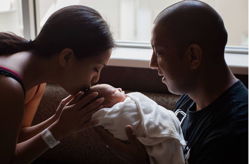 man and woman holding a newborn baby while the woman gives the baby a kiss