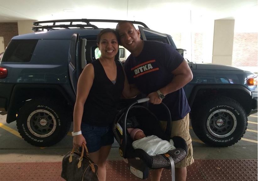 man and woman standing in front of car holding baby in a carrier