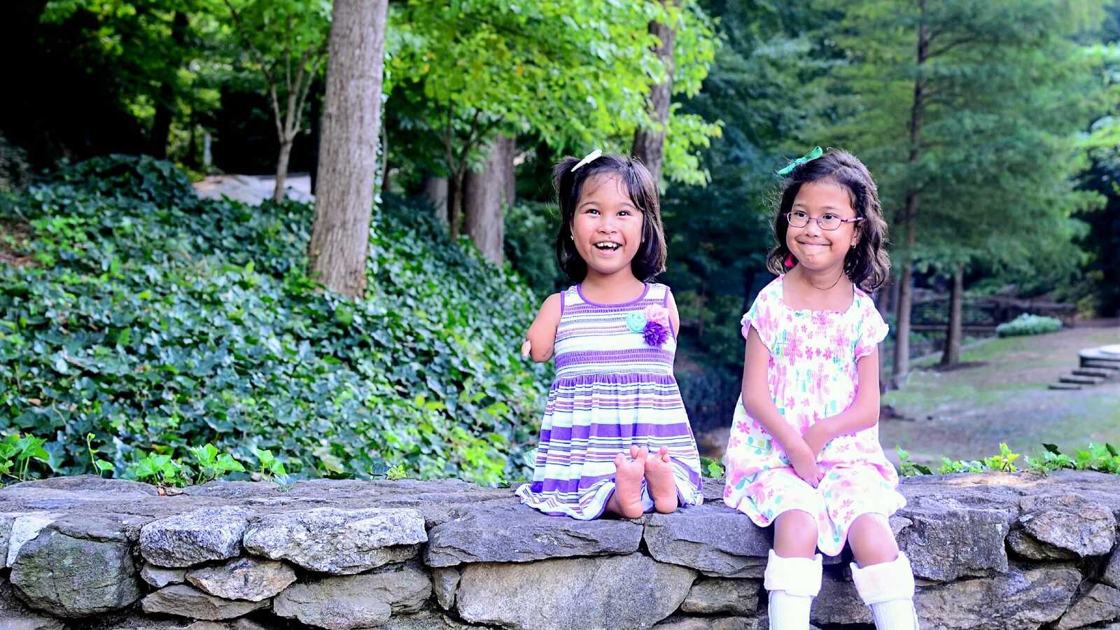 two special needs girls from Thailand smile for photo on stone wall