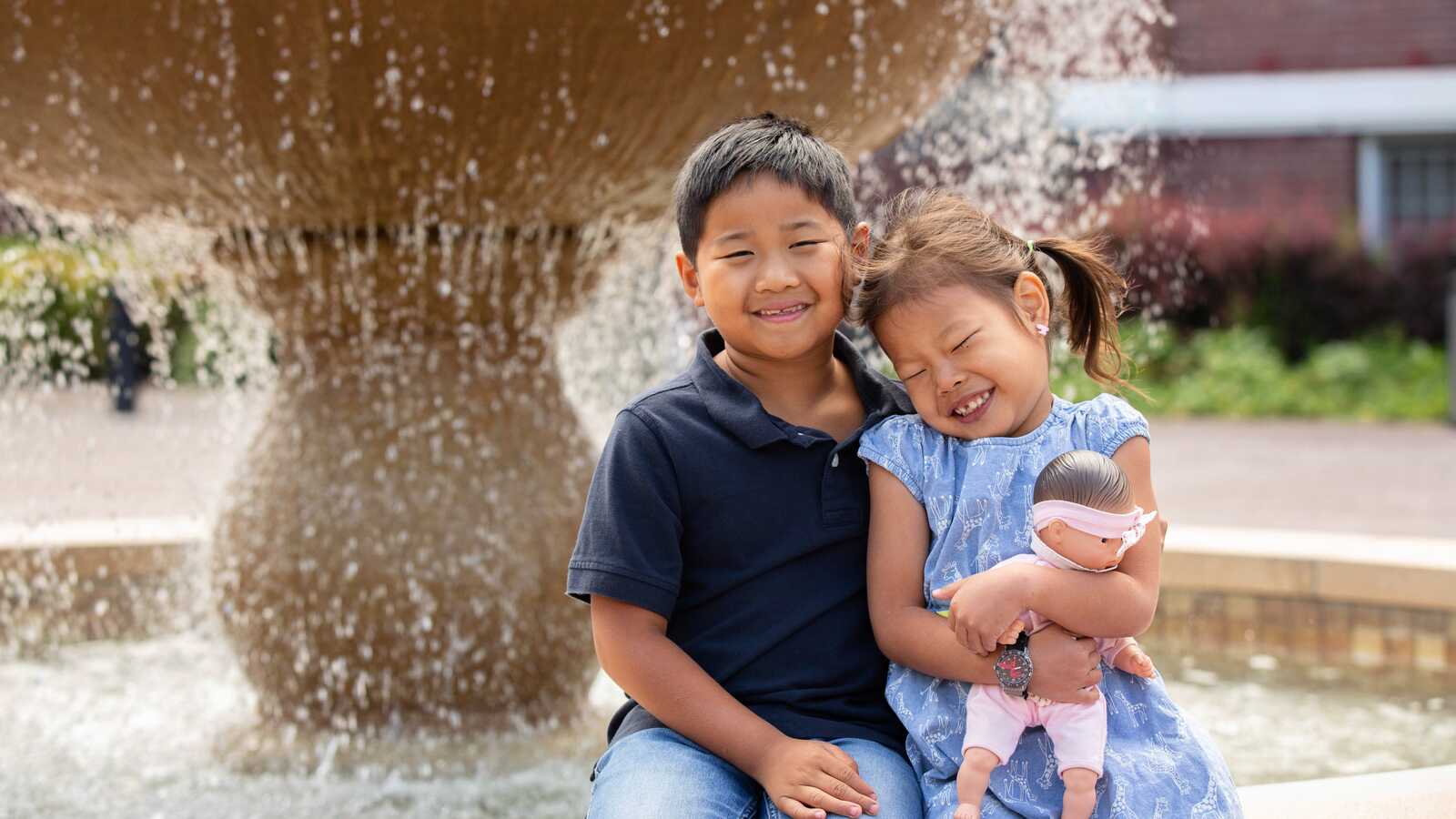 adopted brother and sister laughing at fountain with baby doll