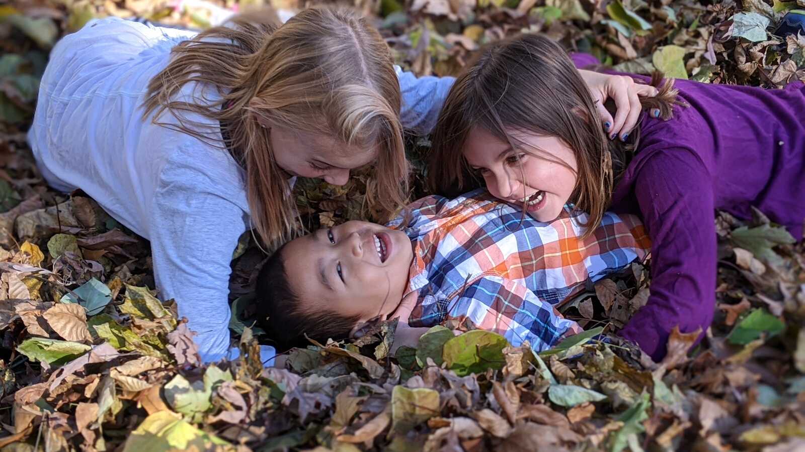 siblings rolling in leaves with adopted brother