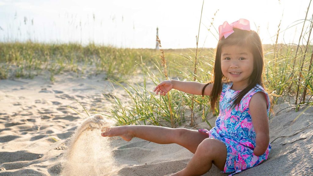 little girl with one arm kicking up sand at the beach