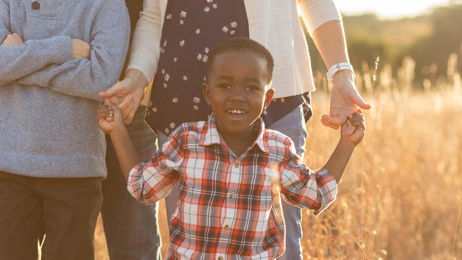 boy adopted from haiti holding adoptive mom's hands in a field