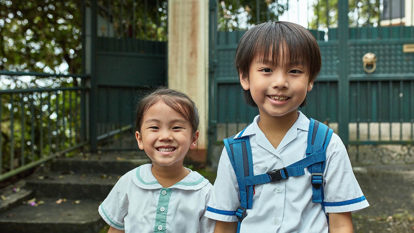 smiling girl next to older brother smiling and wearing backpack