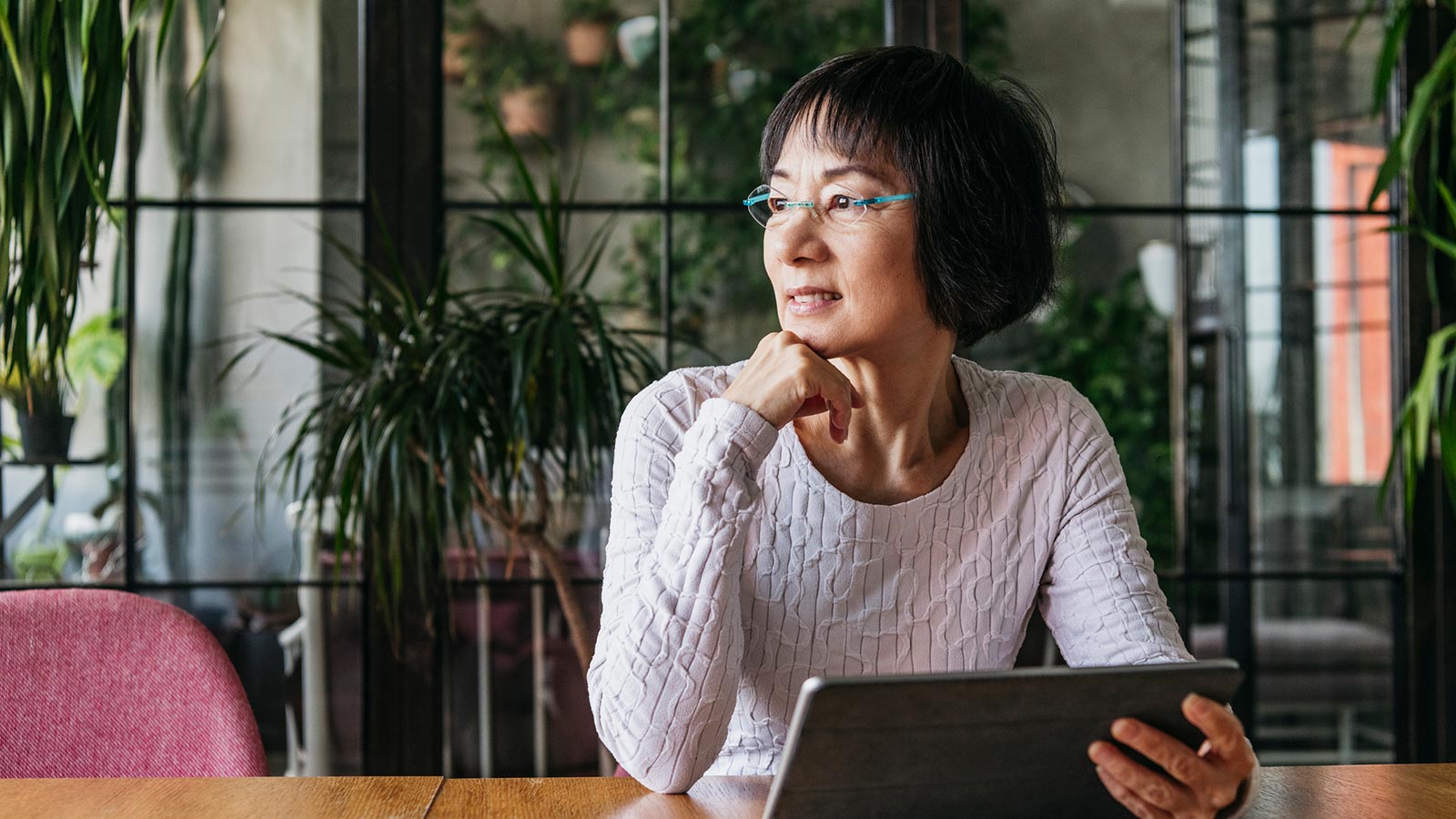 Asian woman looking into the distance wearing blue glasses holding an iPad