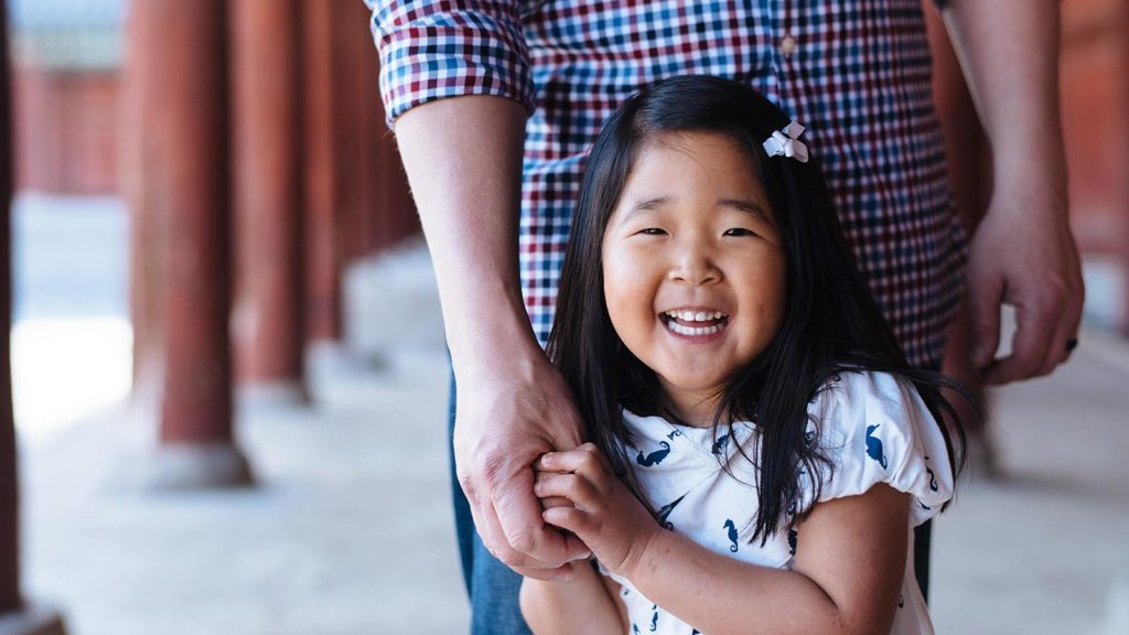 little girl adopted from korea laughing and holding adoptive father's hand