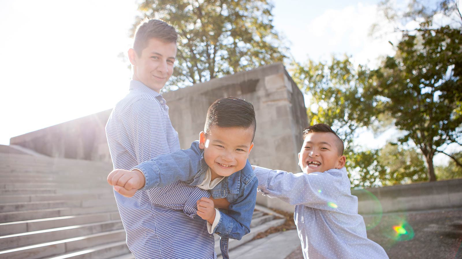 older brother holding younger brother adopted from china making superman fist while other brother laughs