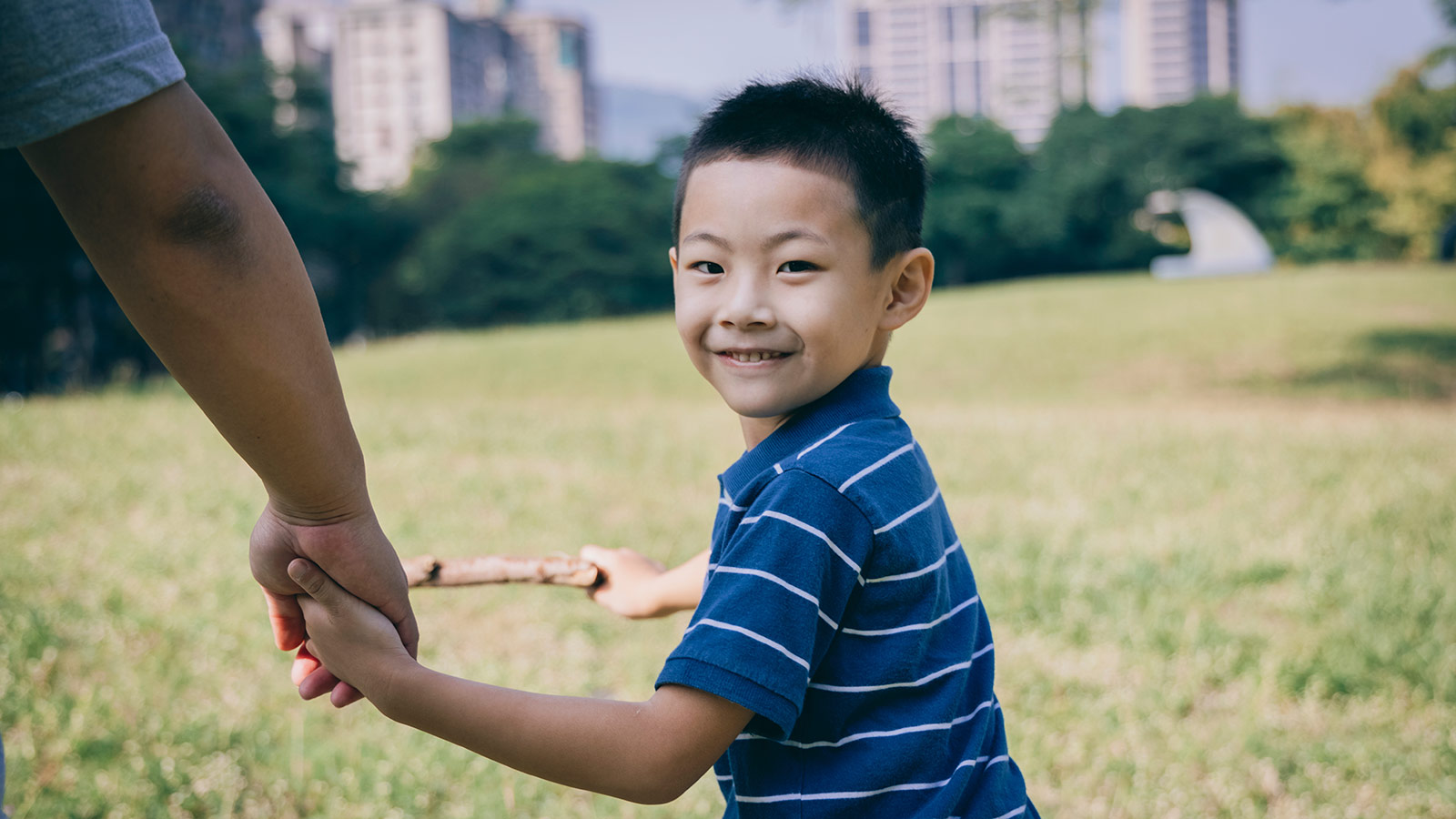 smiling child adopted from taiwan holding parent's hand in grassy park