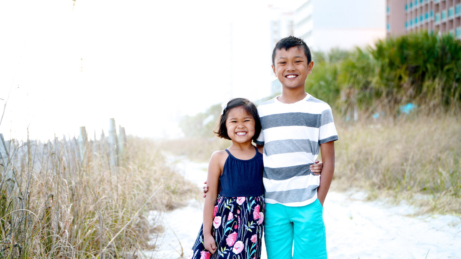 boy and girl adopted from thailand with their arms around each other on the beach