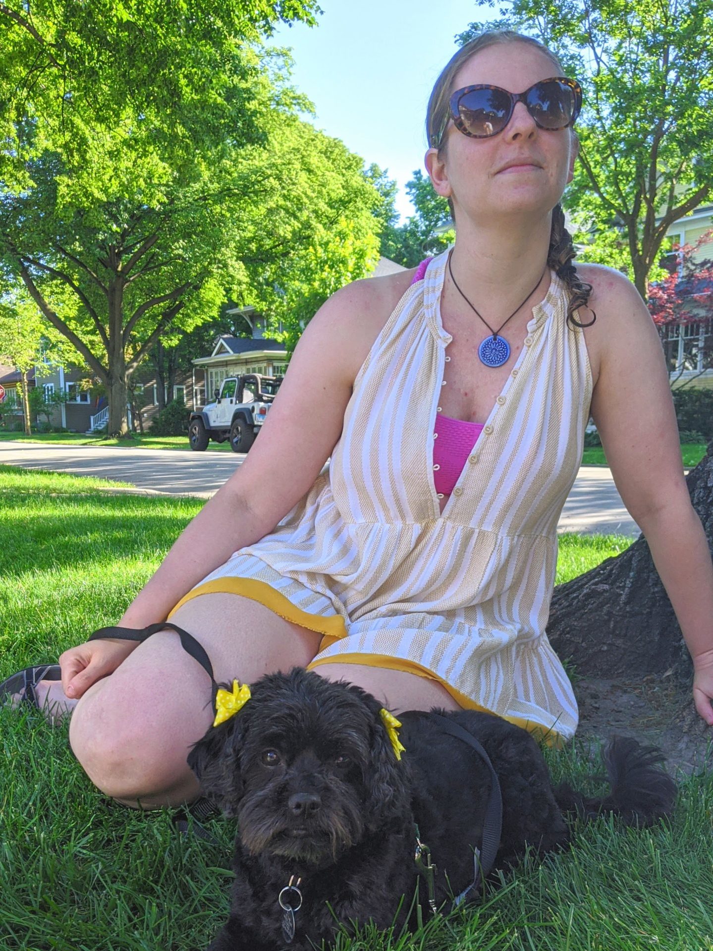 woman wearing sunglasses sitting in the grass with small black dog